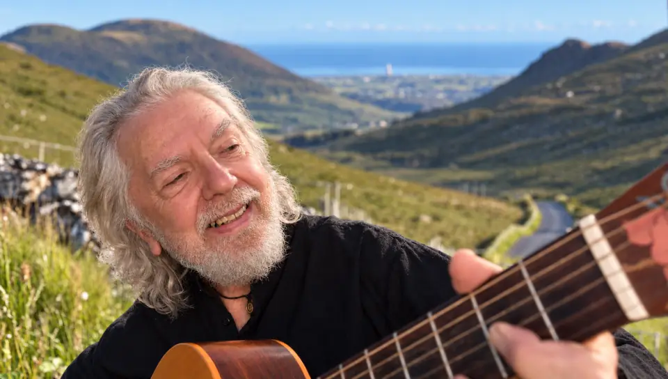 Tommy Sands playing his guitar in the mountains